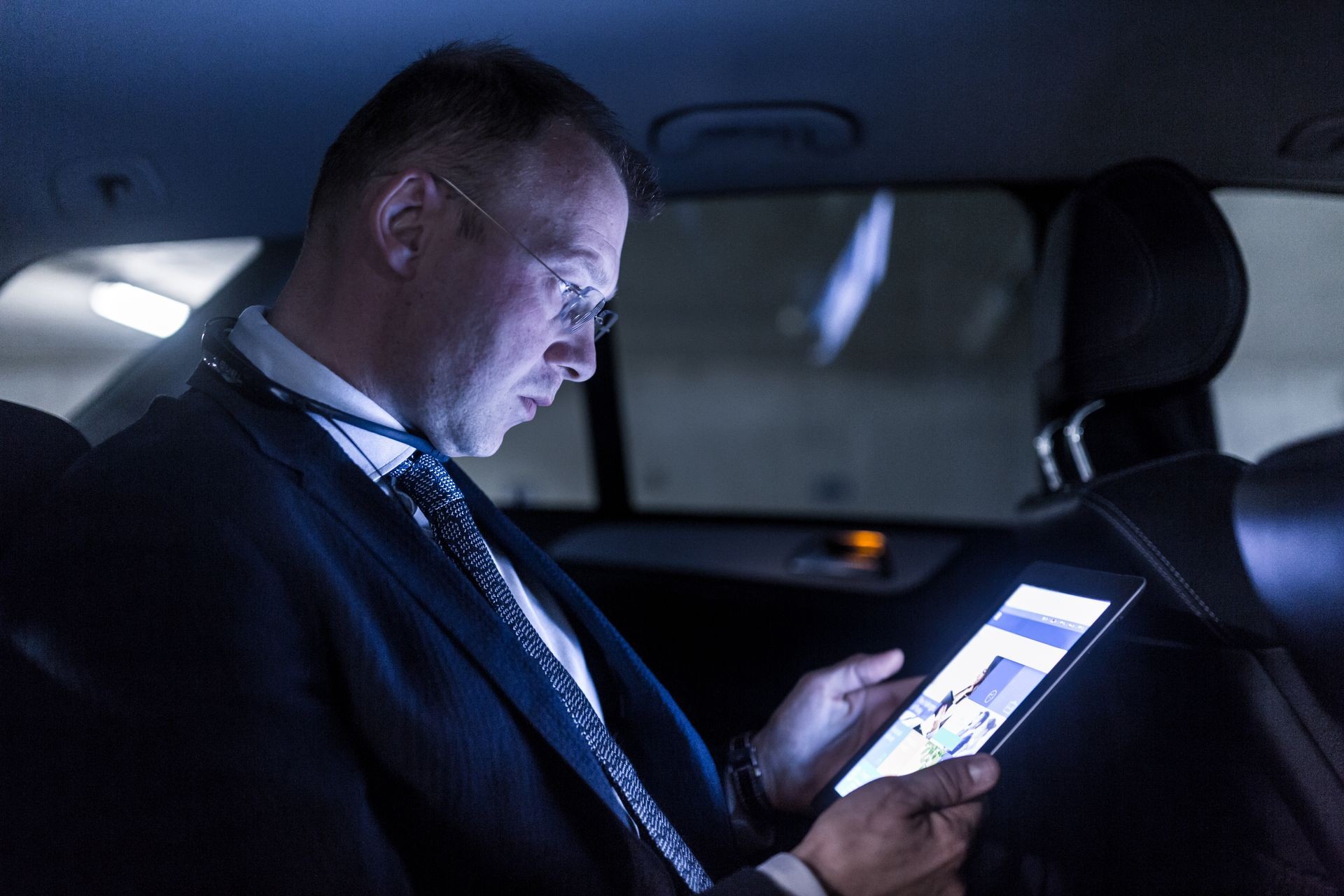 Businessman working remotely on business trip, using digital tablet, sitting in the back seat of taxi car.